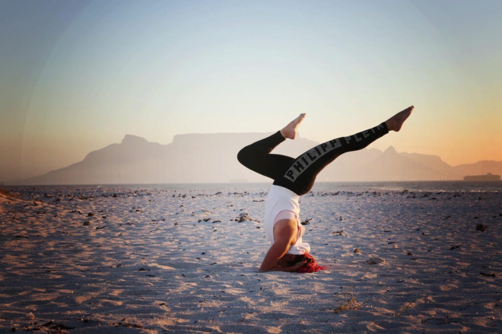 A girl doing a head stand yoga pose on a beach with table mountain in the background